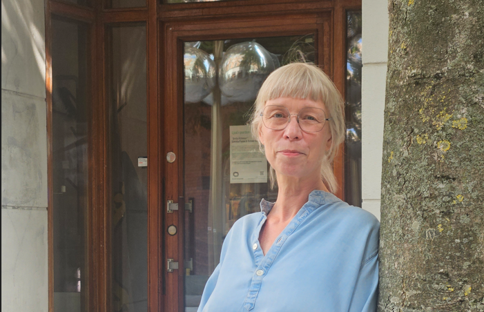 Kvinna med glasögon står utanför en byggnad. Styrelse.