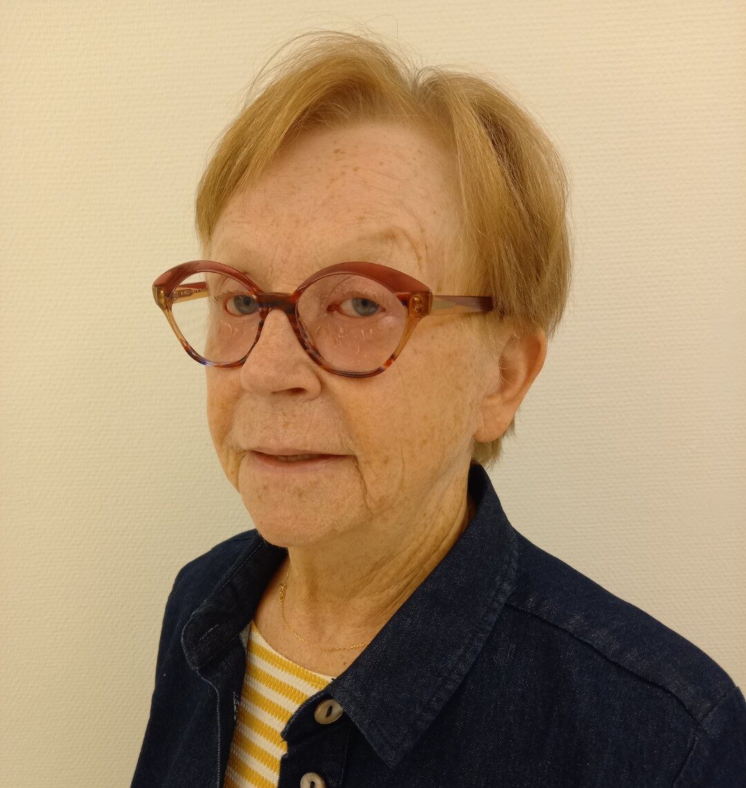 Kvinna med glasögon och kort blont hår, klädd i en blå jacka. Kontakt.