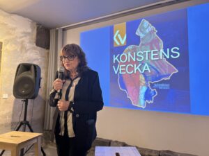 Kvinna talar vid Konstens Vecka-presentation med logotypen på skärmen.