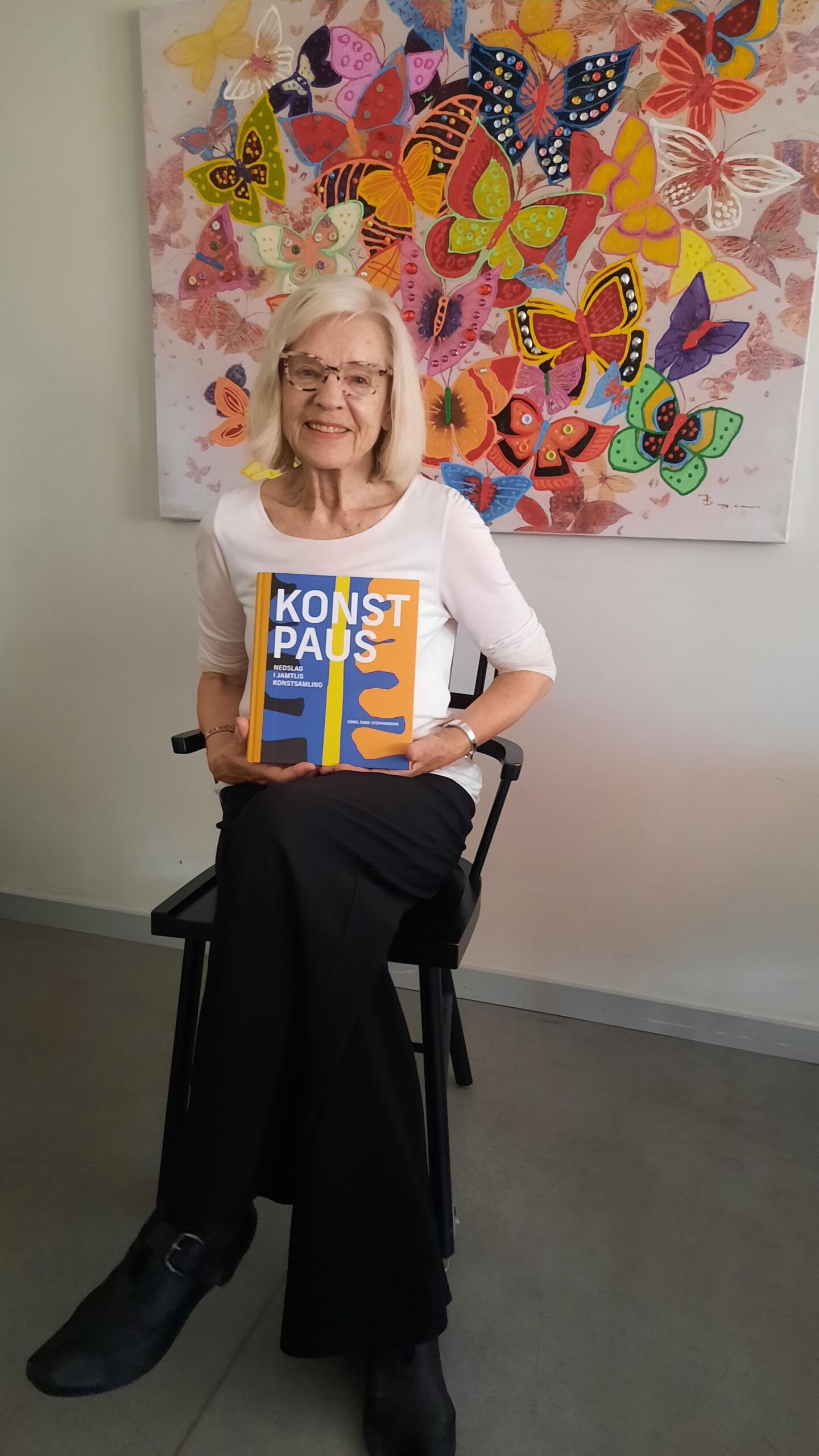 Kvinna sitter med boken "Konstpaus Jämtlands konst". Bakgrund med fjärilar.