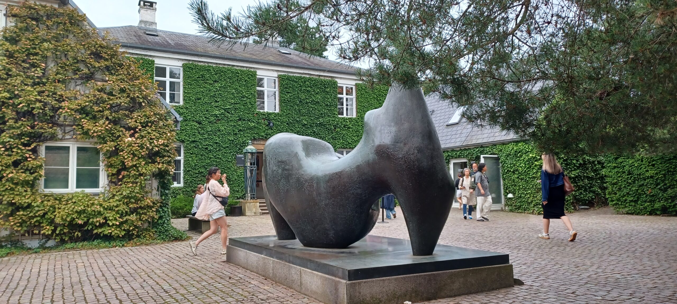 Skulptur framför byggnad täckt av grönska. Dagsresa 10 maj.