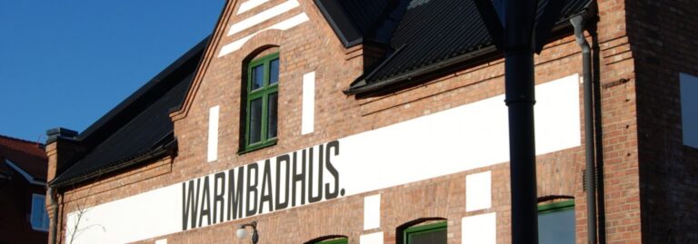 Varmbadhus i Vimmerby, tegelbyggnad med texten "WARMBADHUS" målad på fasaden.