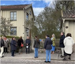 Grupp människor tittar på ett gult hus med staket
